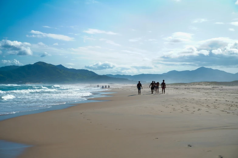 three people walking on the beach next to the ocean