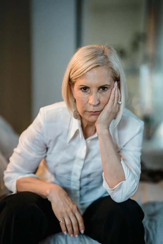 a woman is sitting on a couch holding her hand near her ear