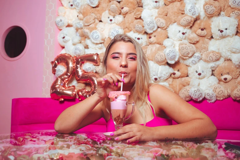 girl drinking champagne while eating pink cupcake in front of large teddy bears