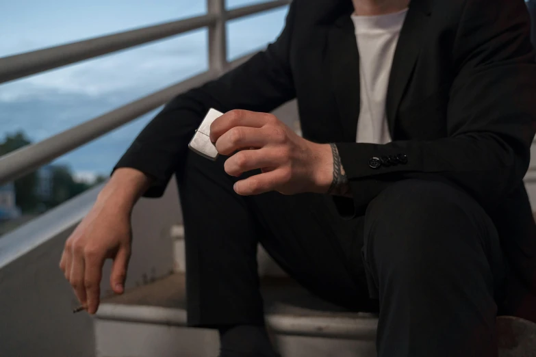 man wearing black suit sitting on a rail holding a white object