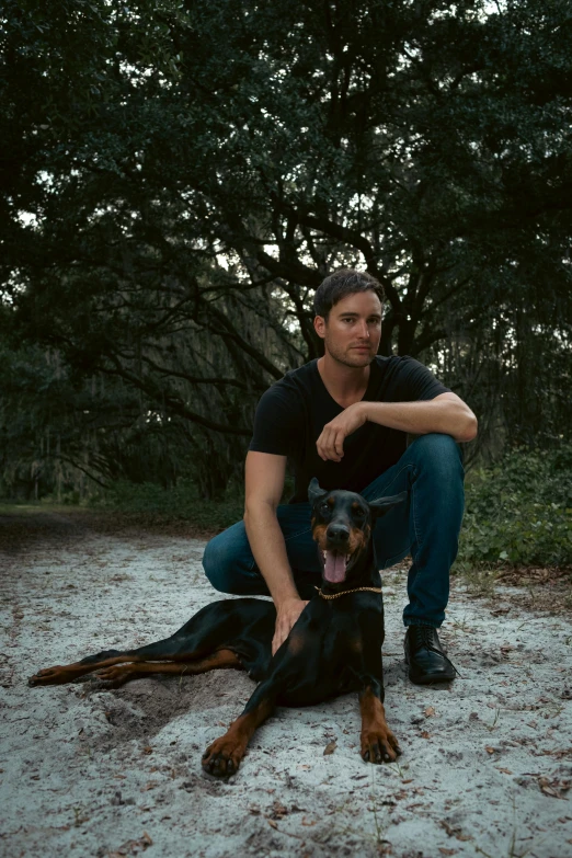 a man poses with a black and brown dog on a path