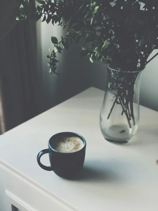 the coffee cup has been placed next to the vase with the flowers