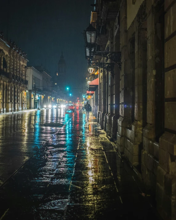 people walk down a sidewalk at night with streetlights on