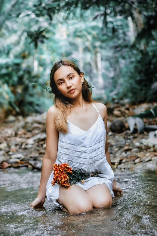 the girl is sitting in water holding a bouquet