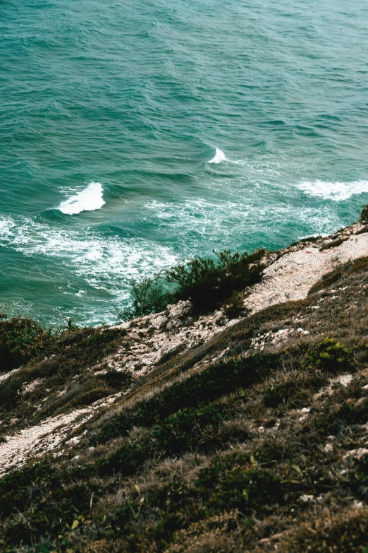 a woman sitting on the edge of a cliff near a body of water