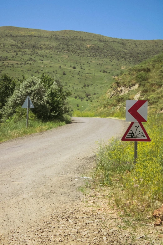 a road sign next to the dirt road on a hill