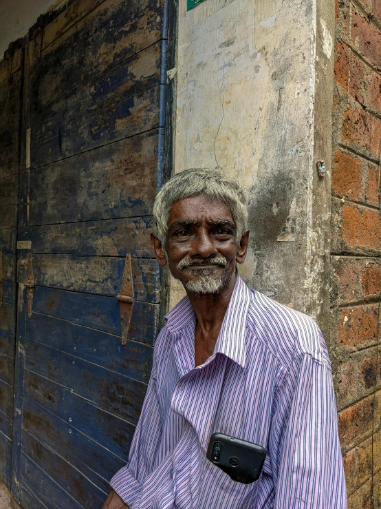 a man with white hair and beard and wearing a purple striped shirt is standing by a building