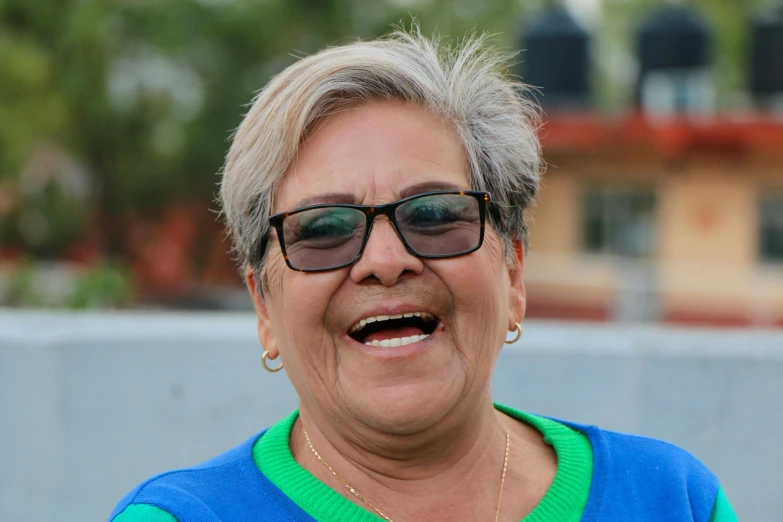 a smiling older woman in sunglasses has her mouth open