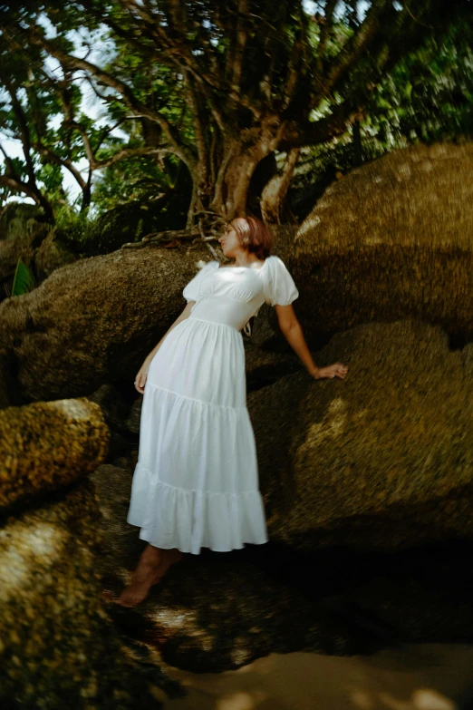 a woman in a dress standing on rocks in the woods