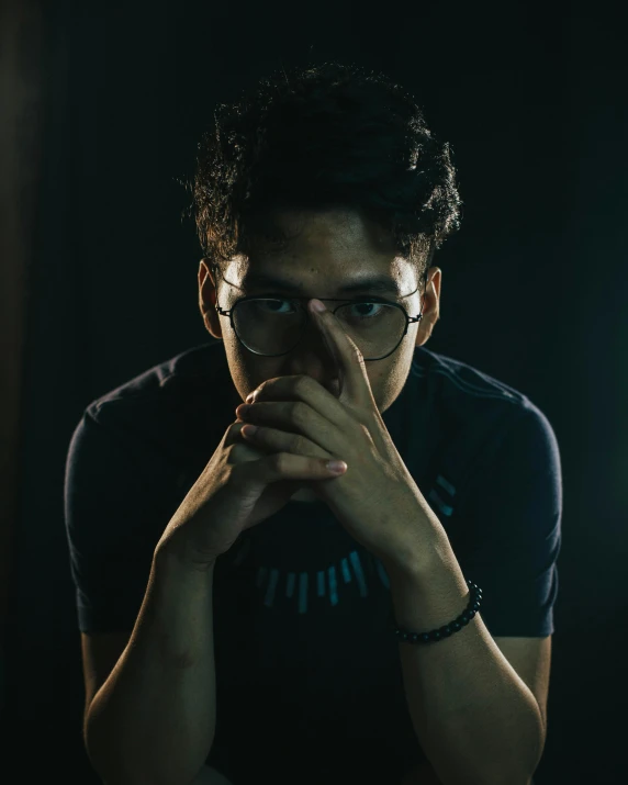 a man posing in a dark room with his hands to his face