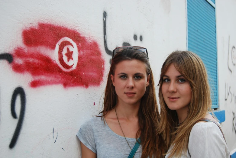 two beautiful women standing next to each other near graffiti