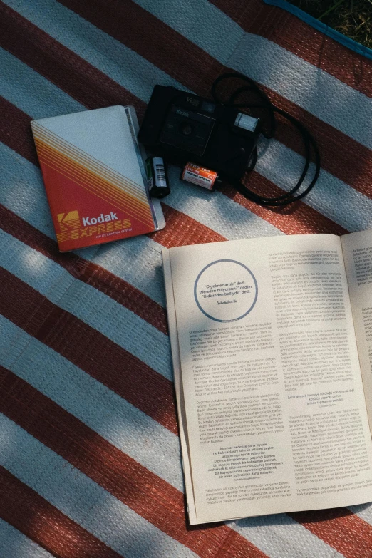 open book laying on red and white stripe rug next to a camera