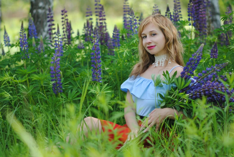 a beautiful young woman is sitting in a field full of purple flowers