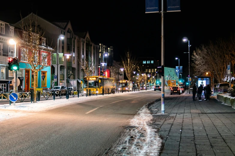 the sidewalk is littered with snow while traffic light in the background shines on the street