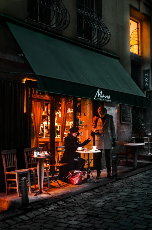 three people sitting at tables under a green awning