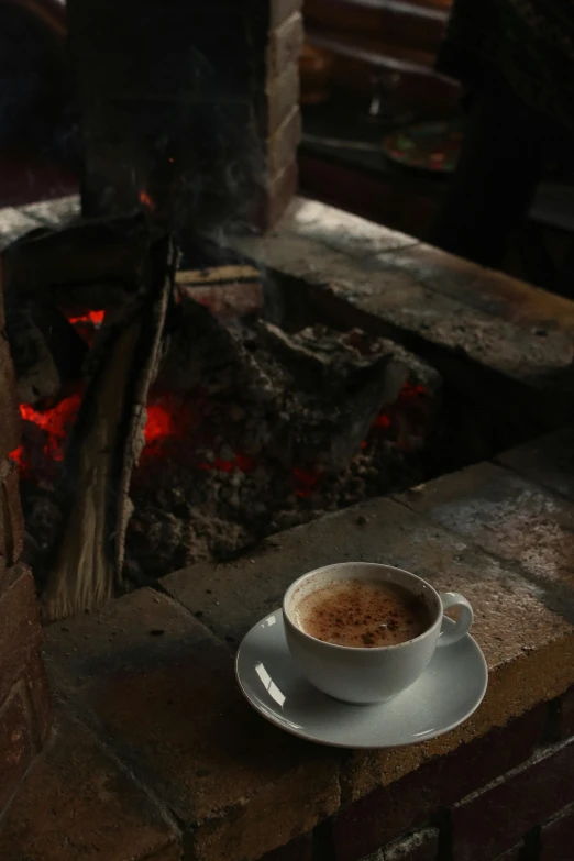 a cup of coffee sitting on a saucer in front of a fire