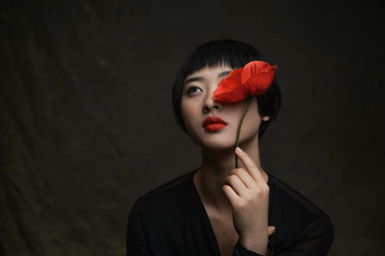 woman holding red flower with one eye opened to the side