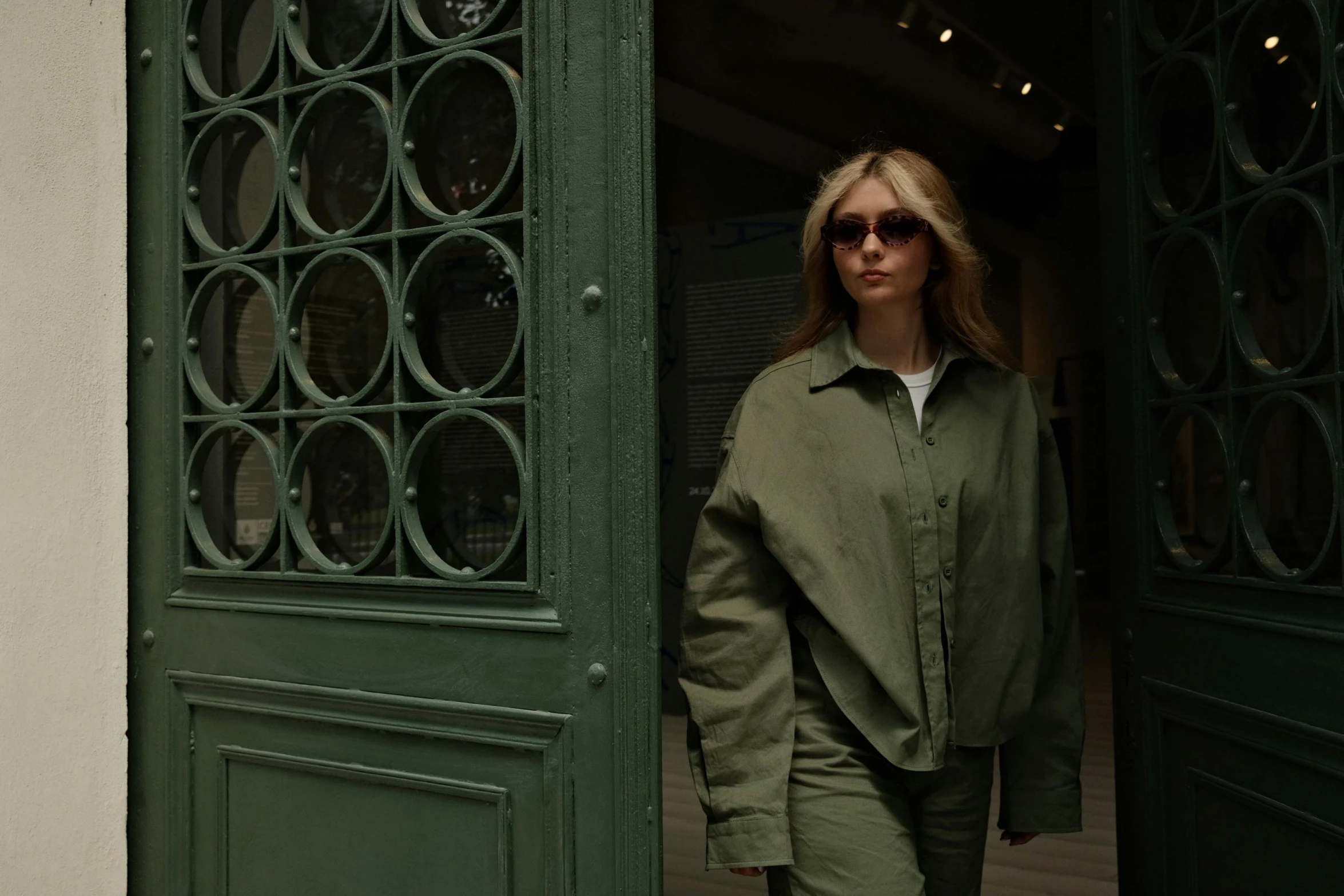 a woman wearing a green jacket stands at an open door