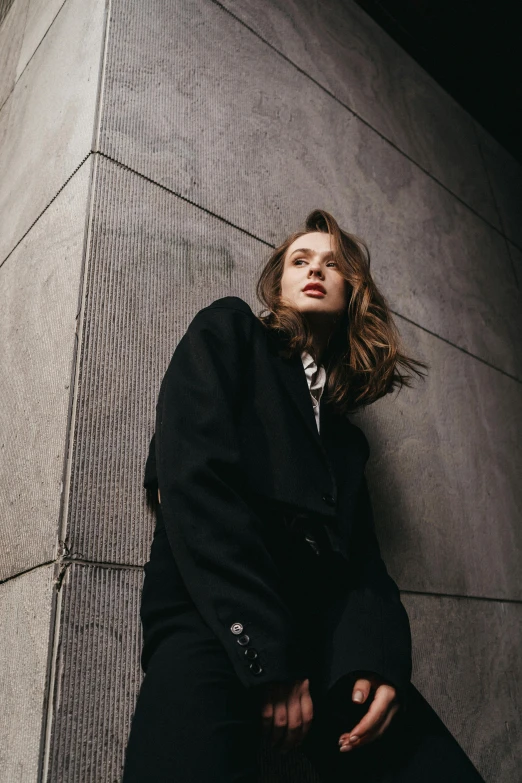 a woman leaning against a building next to a stone wall