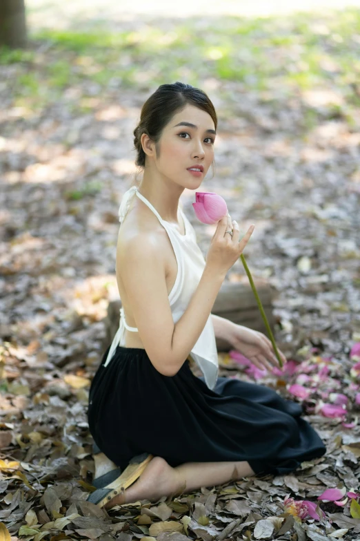 young woman in white tank top sitting on ground with rose