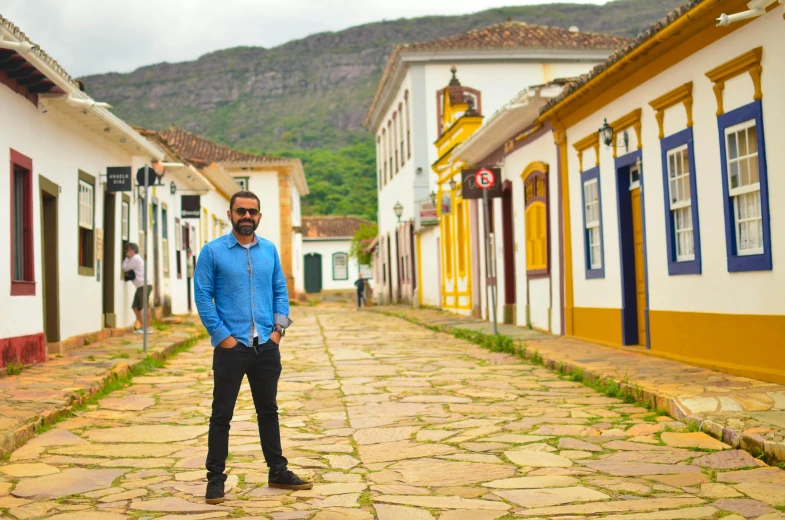 a man stands in a cobblestone street that has several buildings painted white and blue