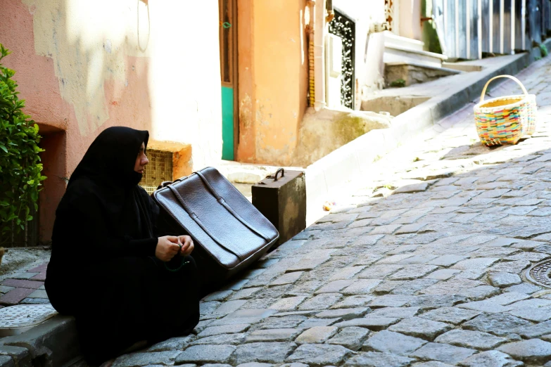 woman sitting on the ground holding suitcase next to street