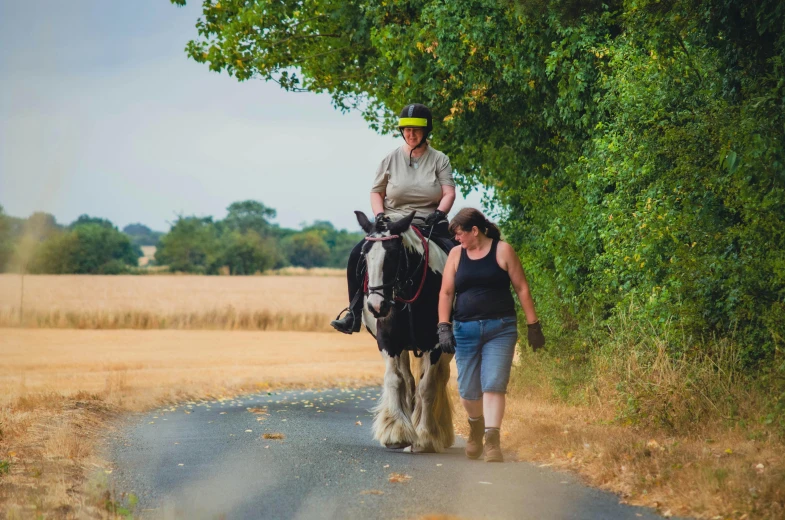 a woman walks along a path while a horse pulls a wagon