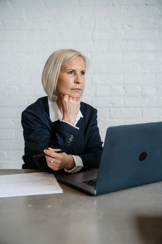 woman looking at laptop while sitting at desk in front of brick wall