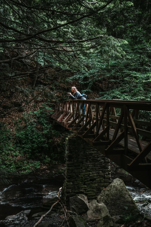 a man and woman standing on a wooden bridge crossing a creek