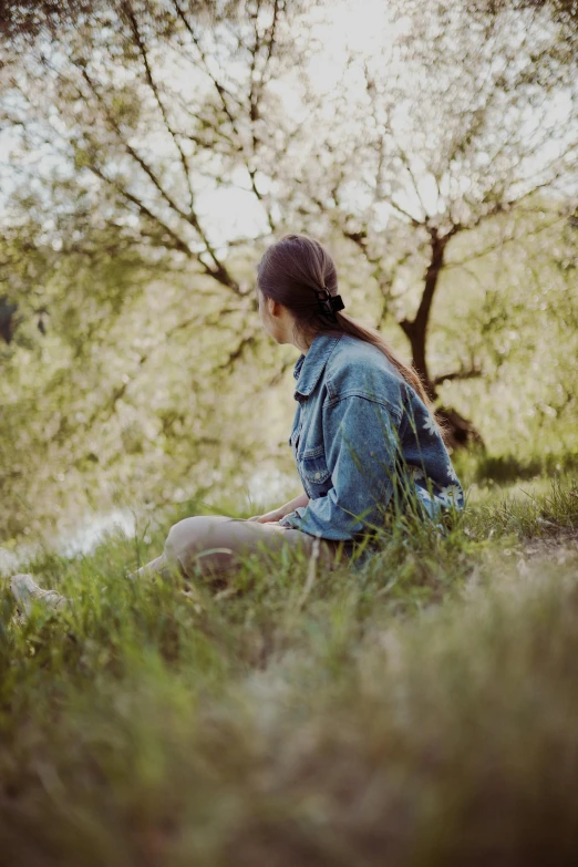 a woman in a denim dress sits on the grass with a bird in her hand