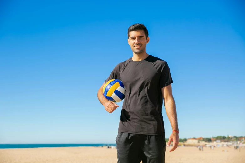a smiling man holds up a volley ball