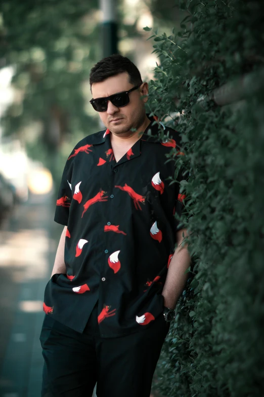 man leaning against the wall, dressed in sunglasses