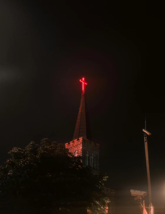 an illuminated red cross atop the steeple of a church