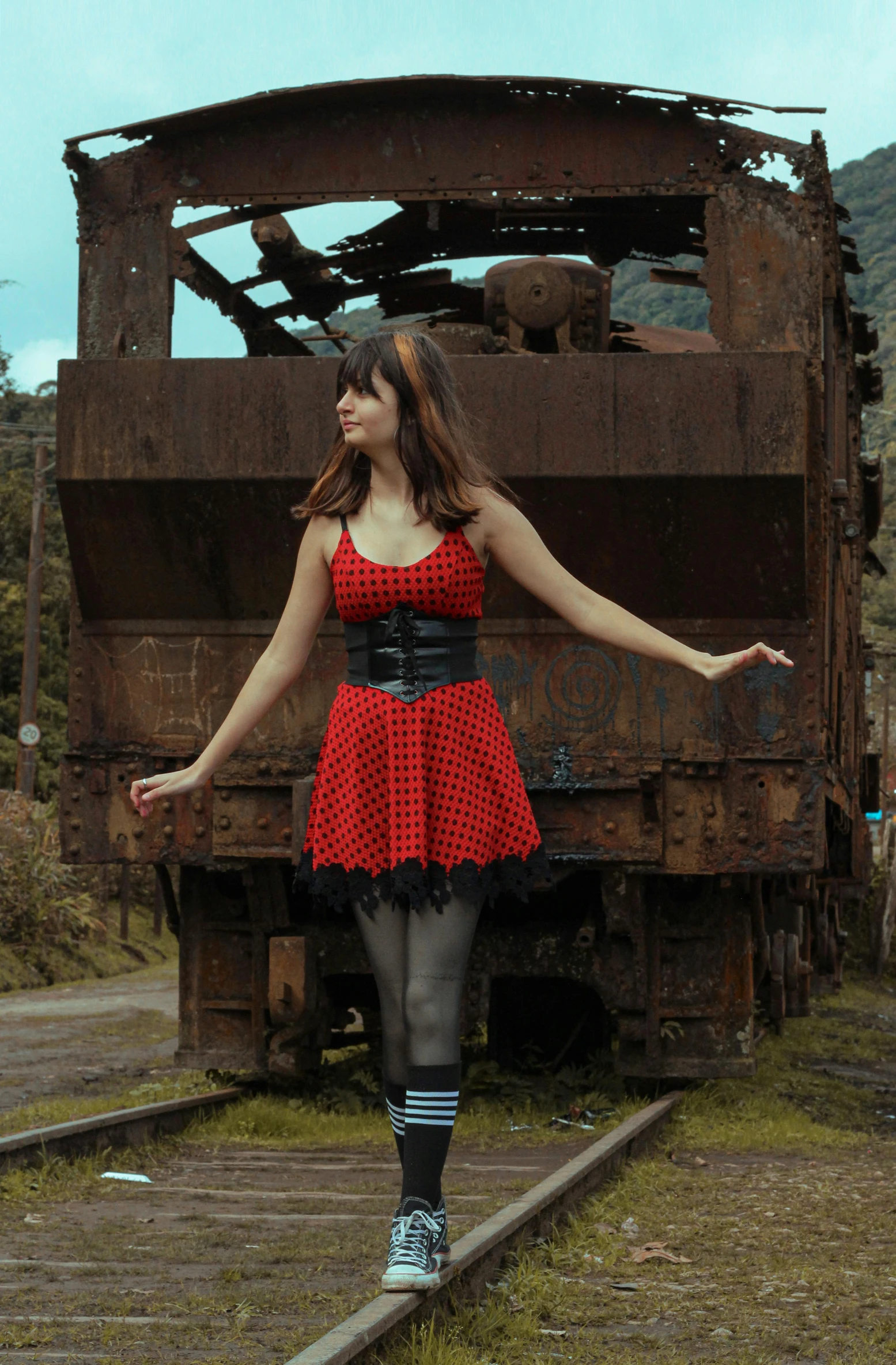 a woman dressed in red and black in front of a rusted out train