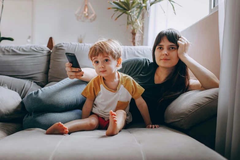 a woman and child sitting on a couch looking at a phone