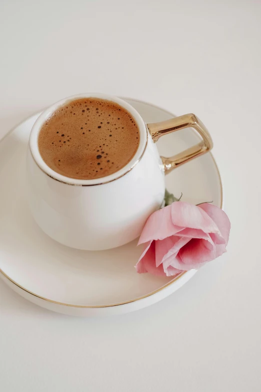 a rose rests on a saucer next to a cup of coffee
