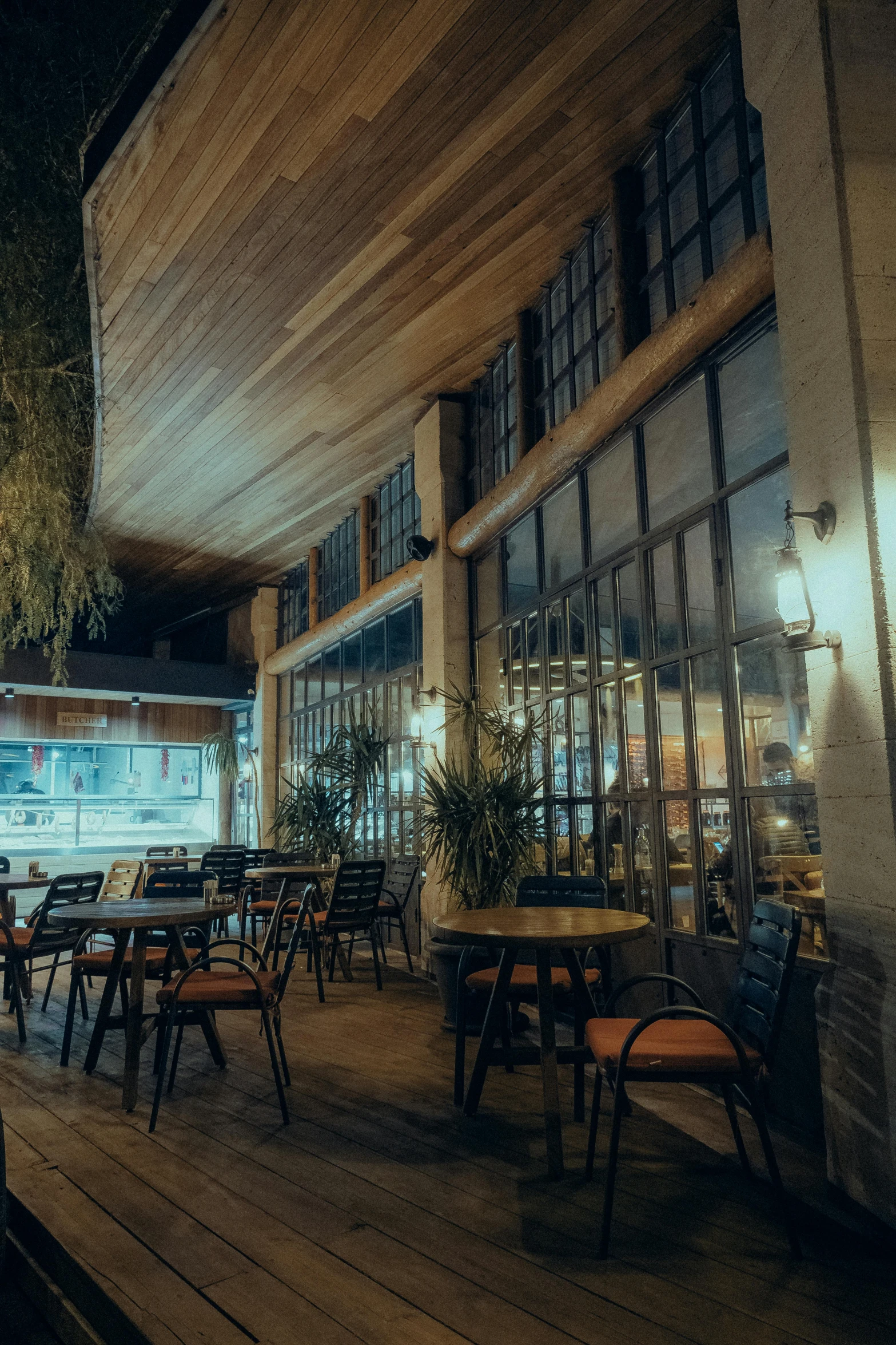 a restaurant with tables, wooden chairs and green plants