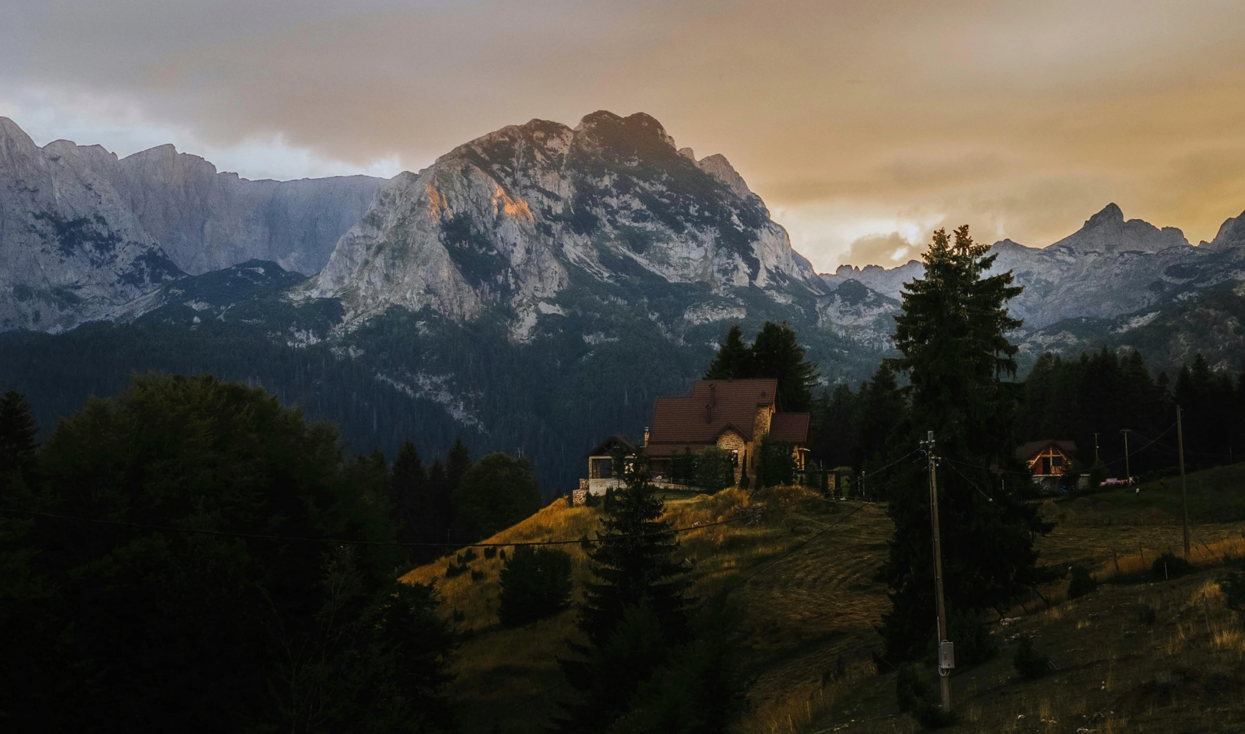 a landscape pograph of houses on a green hillside with the mountains in the background