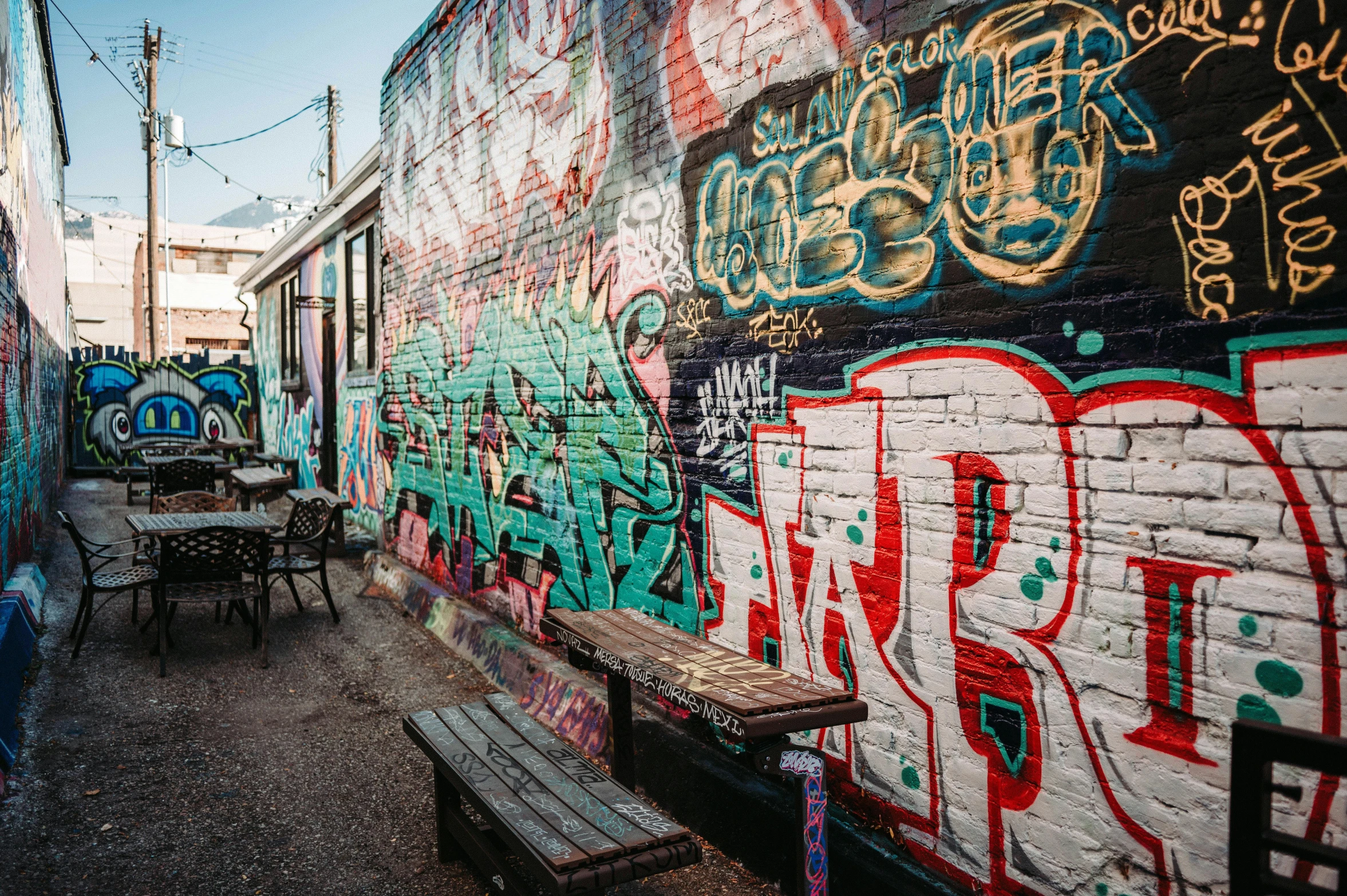 the back wall of an outside restaurant with tables and chairs, graffiti on it