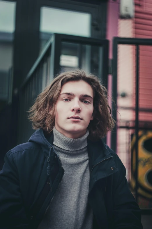 a man with long hair standing next to a building