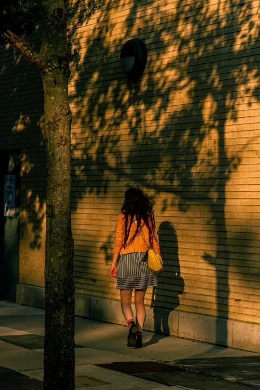 a person wearing an orange jacket and striped skirt walks down the sidewalk