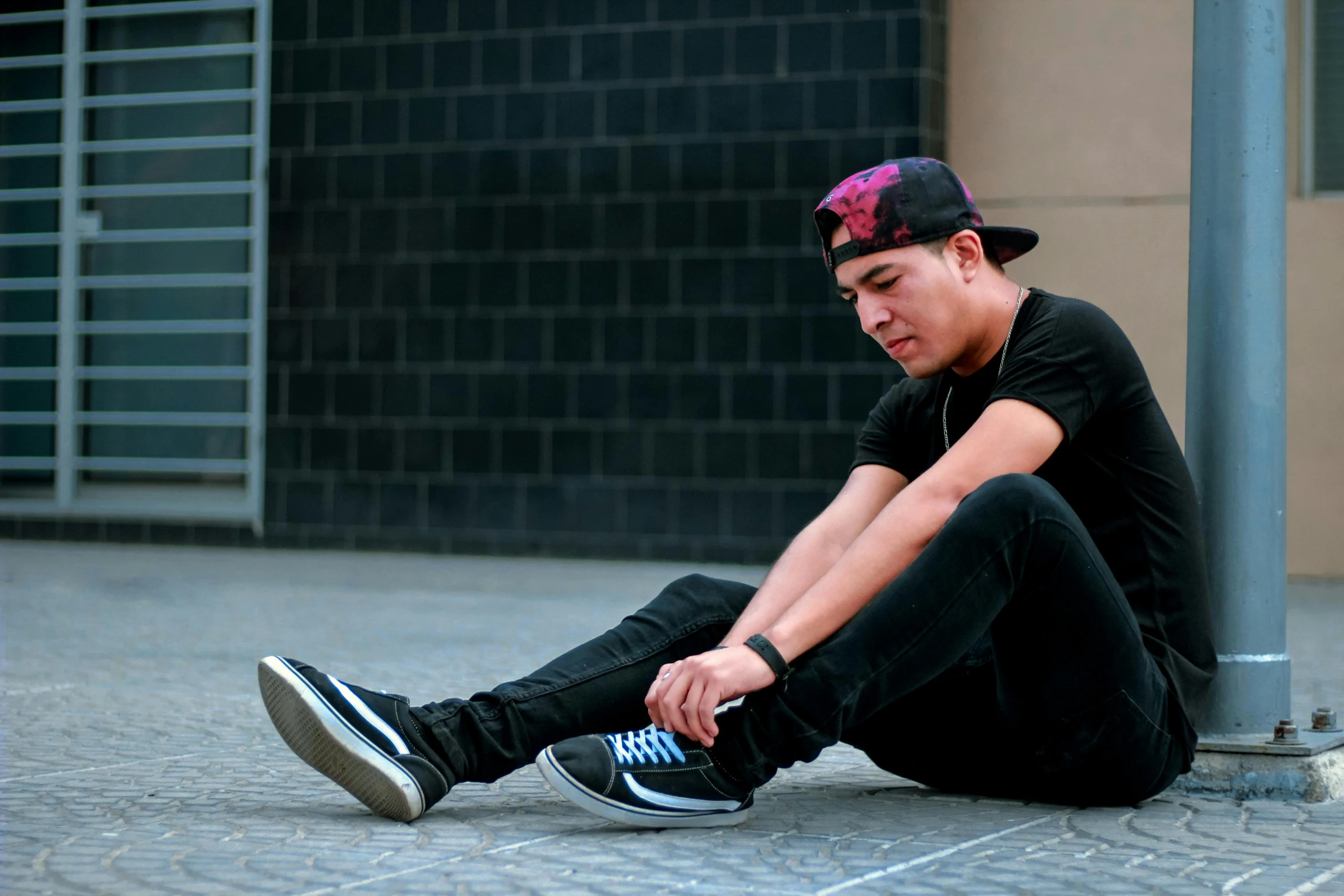 a young man sits against a pole on the ground