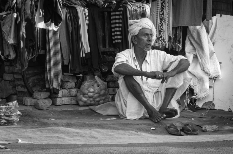 black and white image of a man sitting down in front of clothing store