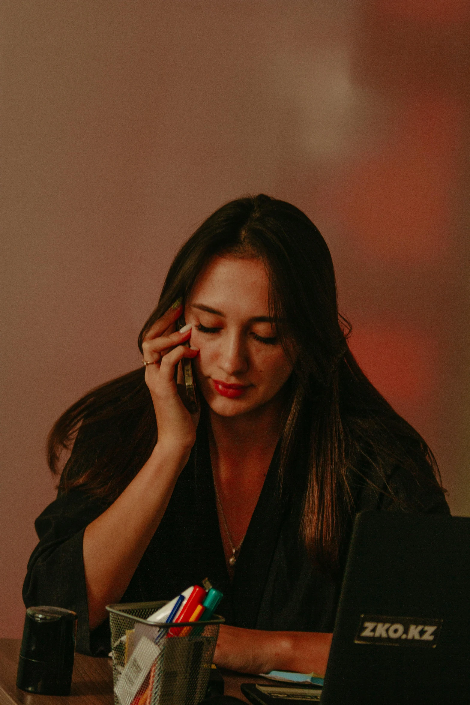 a woman on her cell phone at a desk using a laptop computer