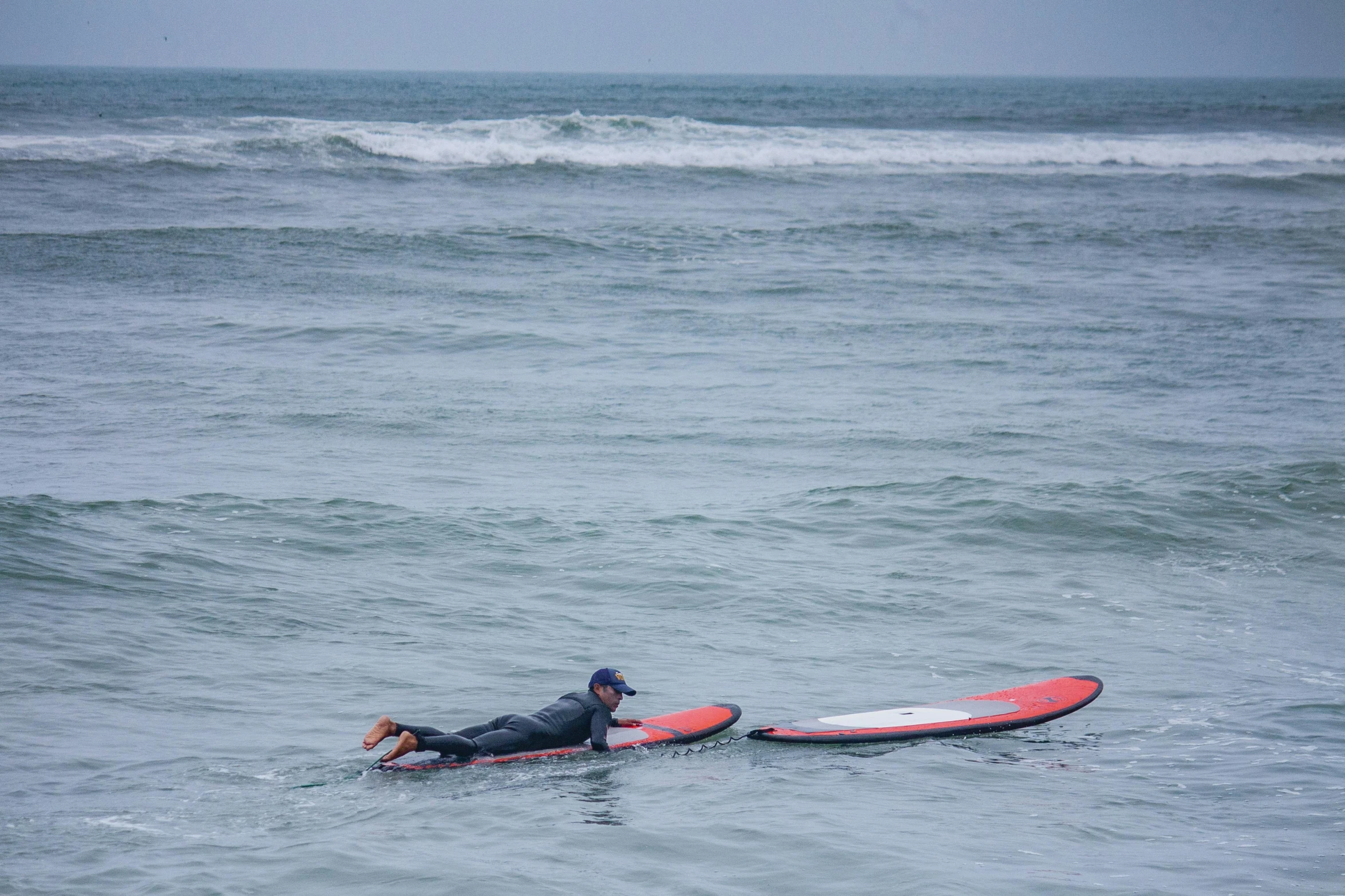 two surfers in wet suits riding boards into the ocean