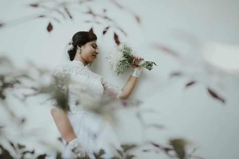 a woman in white holds flowers near some leaves