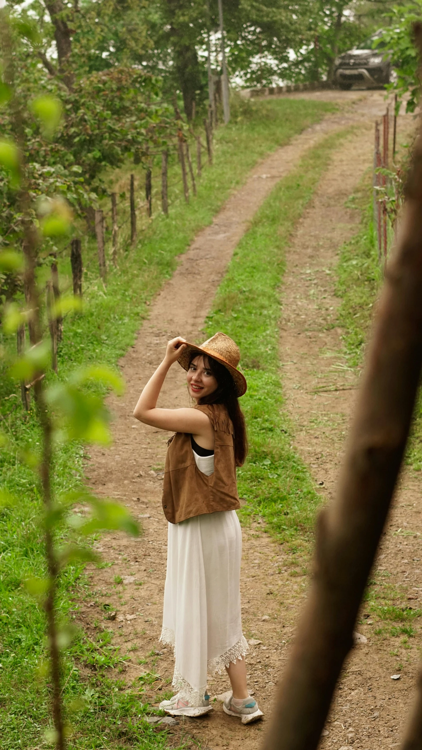 a woman wearing a brown hat stands on a dirt road