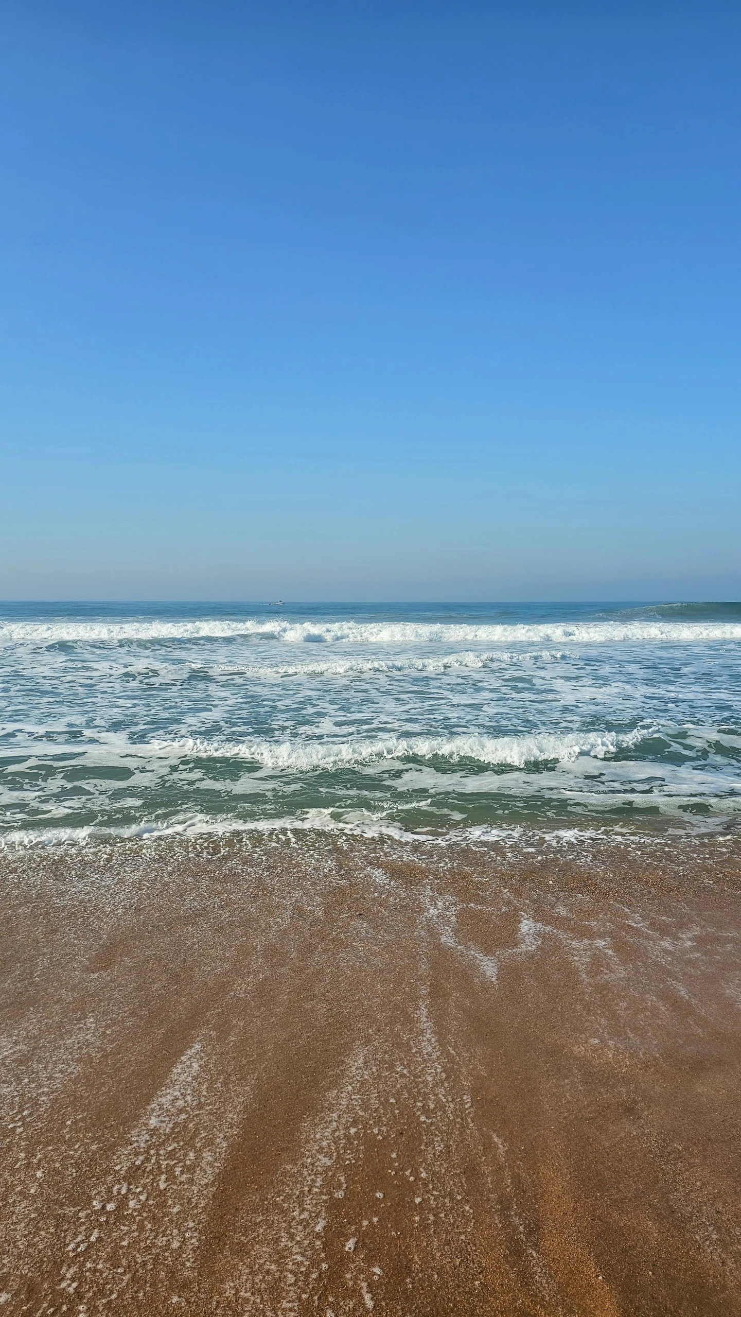 a sandy beach with waves and blue skies