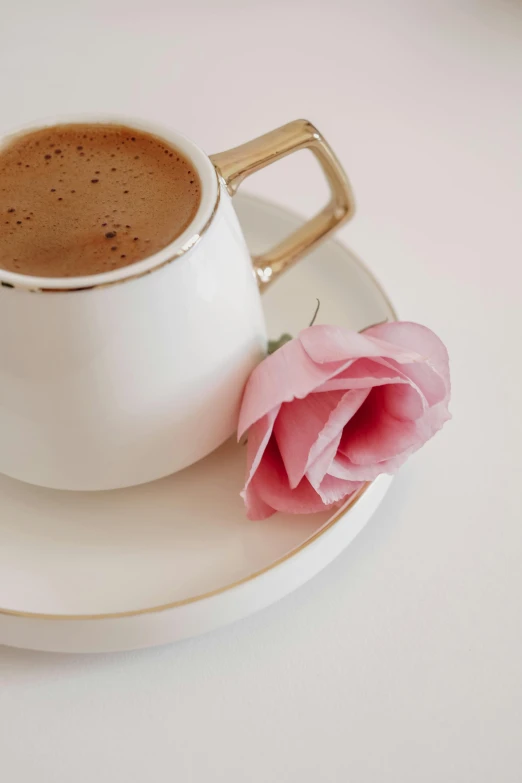 a small pink flower on a saucer with a cup of coffee