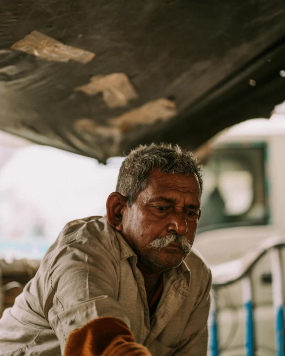 an older man with moustache on his head, leaning against the back of a truck